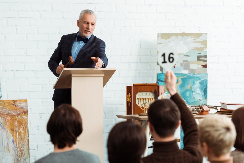 selective focus of auctioneer holding gavel and pointing with finger at buyer during auction