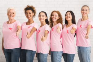 Ladies With Breast Cancer Ribbons Gesturing Thumbs-Up Standing Over Wall